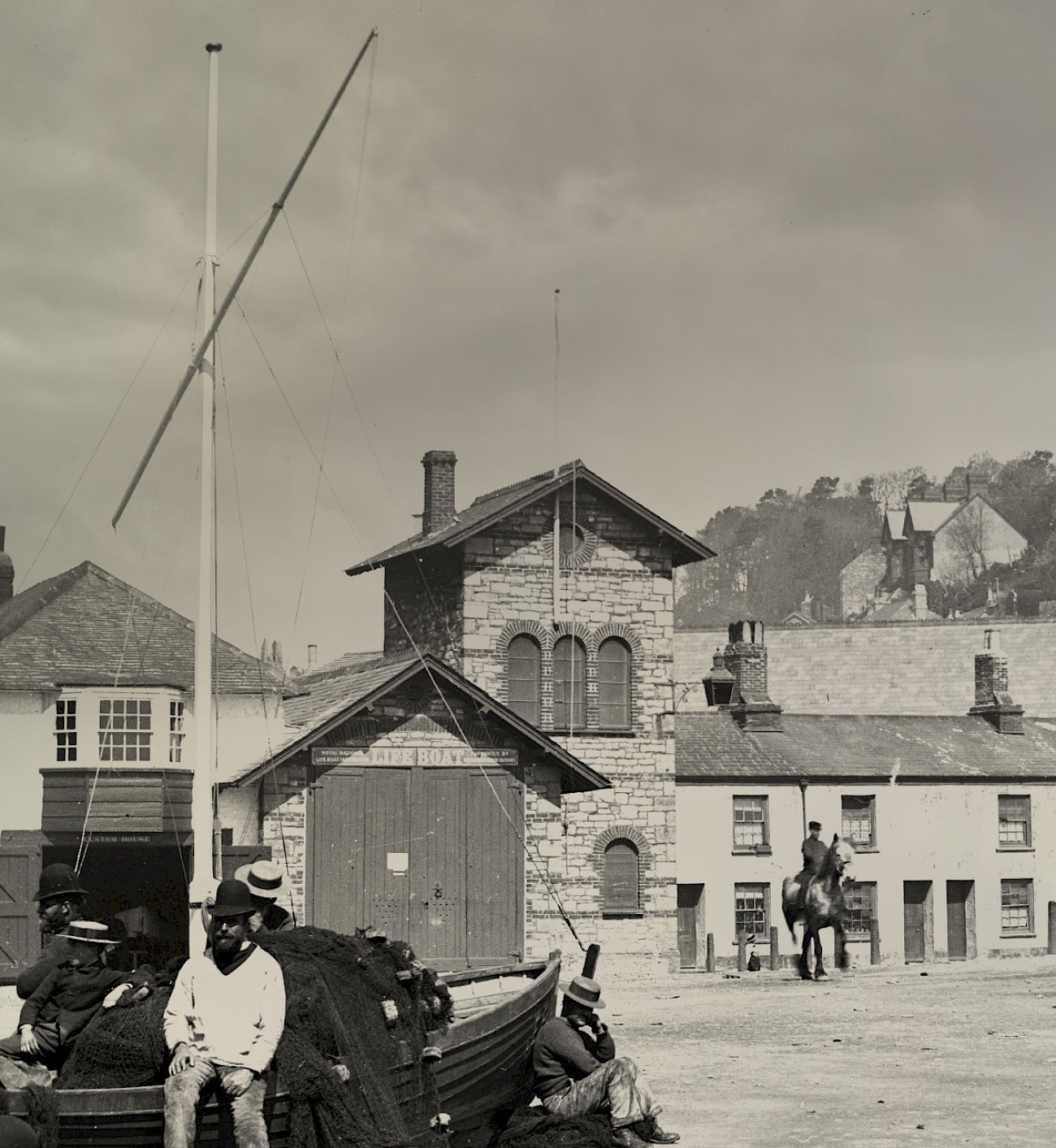 Victorian fishermen mend their nets with the old lifeboat station in the background.
